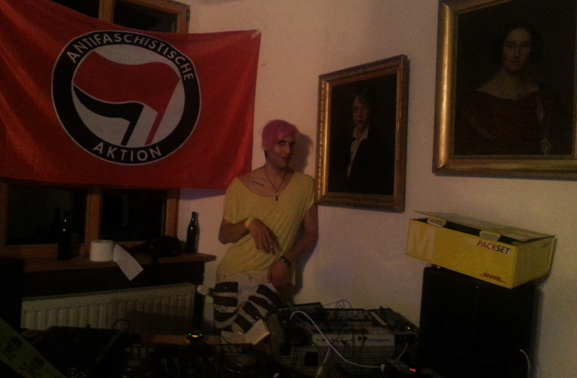 Phant hinter dem DJ-Pult, zwischen Antifa-Fahne und Ahnenportraits.